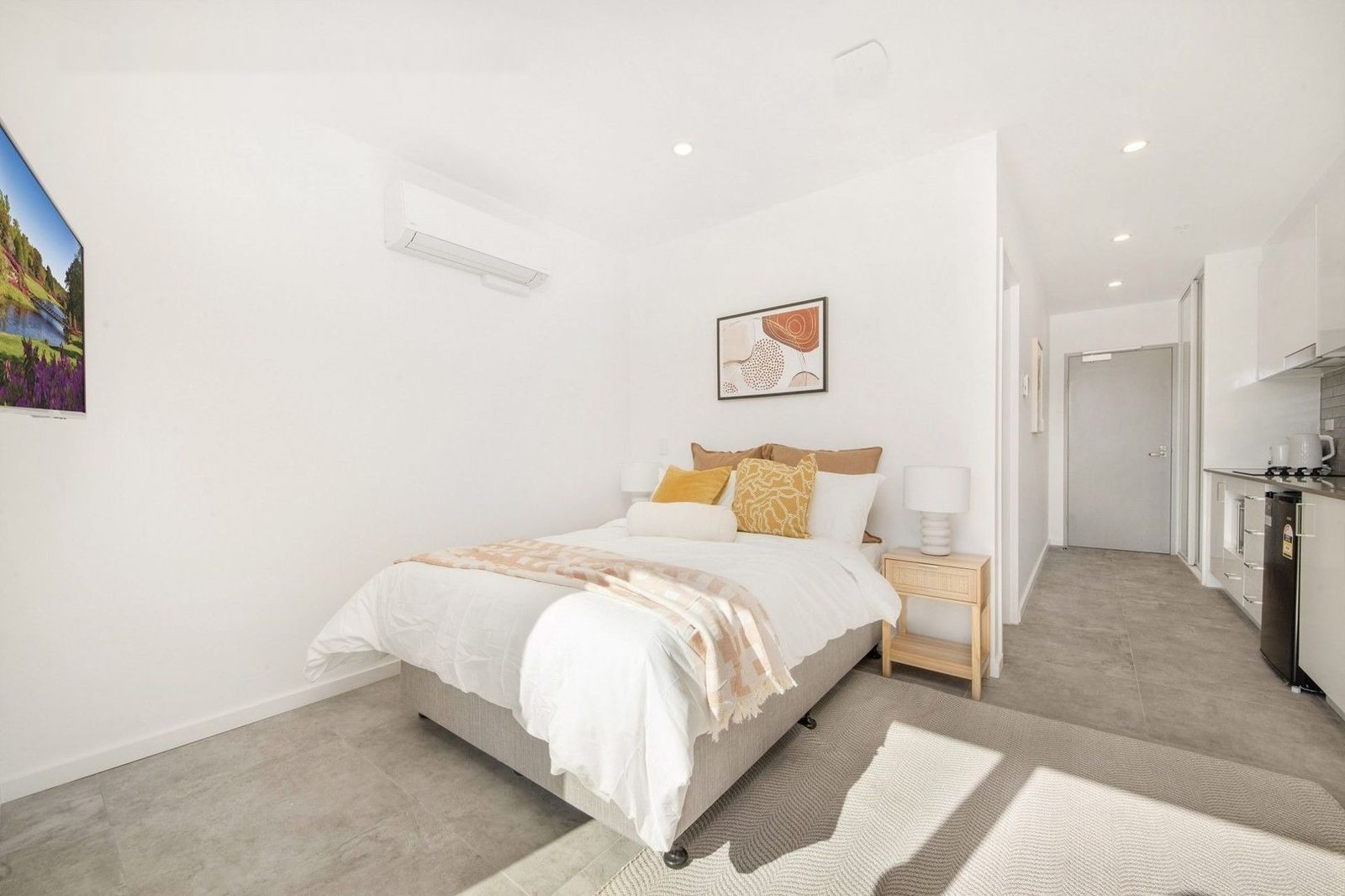 A warm, styled studio bedroom with a queen bed, soft linens and natural light